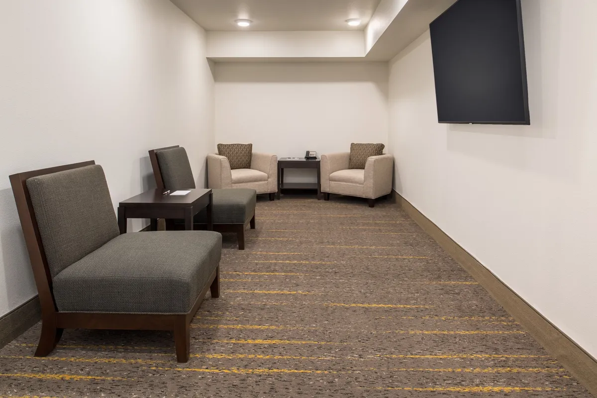 A cozy seating area is displayed, with two armchairs and a small table placed in front of a television. This intimate corner is ideal for relaxed conversations, brief meetings, or quiet work sessions, aligning with the concept of having quiet, laptop-friendly workspaces on-site.