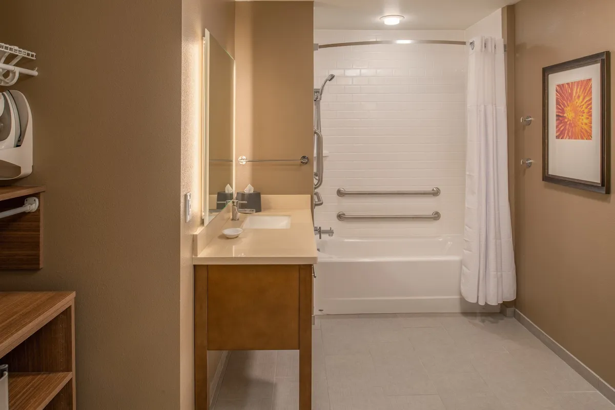 A soothing bathroom scene with a well-lit vanity, a bathtub, a large mirror, and decorative artwork. The space is serene and designed for relaxation and refreshment after a busy day.