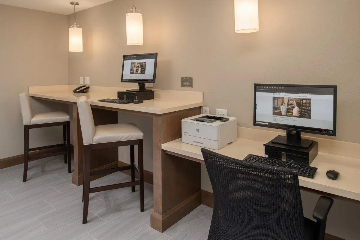 A modern workspace featuring computers, a printer, bar-height seating, and stylish pendant lighting. The area is designed for productivity, offering technology and a comfortable setting for work or studying.